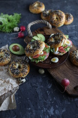 Bagels with salmon, avocado and green lettuce on a wooden board. Breakfast with light healthy snacks.
