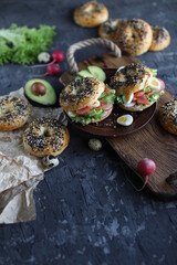 Bagels with salmon, avocado and green lettuce on a wooden board. Breakfast with light healthy snacks.