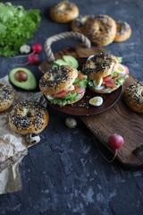 Bagels with salmon, avocado and green lettuce on a wooden board. Breakfast with light healthy snacks.