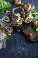 Bagels with salmon, avocado and green lettuce on a wooden board. Breakfast with light healthy snacks.