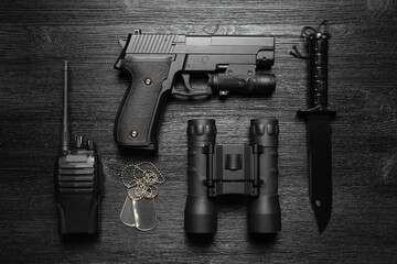 Black airsoft gun, walkie talkie radio station, binoculars, knife and soldier badge on the black...