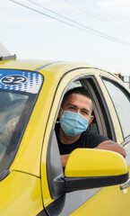 Latino taxi driver sitting inside his yellow car ready to work all day, wearing a mask for...