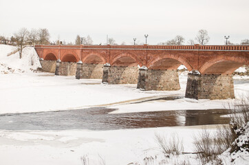 Long brick bridge over Venta river in winter day, Kuldiga, Latvia.