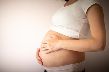 Pregnant woman wearing a white t-shirt with hands on belly on blank background. Background with copy space. Profile, side view.