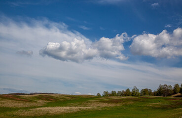 Obraz premium Hilly area with trees growing on it. Most of the frame is taken by the sky with beautiful clouds.