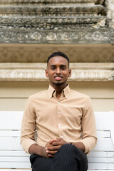 Handsome African businessman sitting and smiling outdoors in the city
