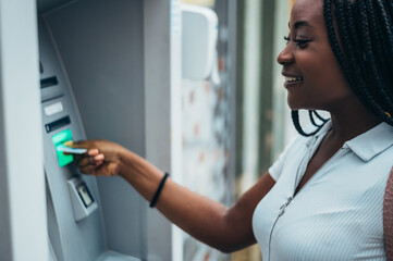 Cheerful african american woman using credit card and withdrawing cash at the ATM