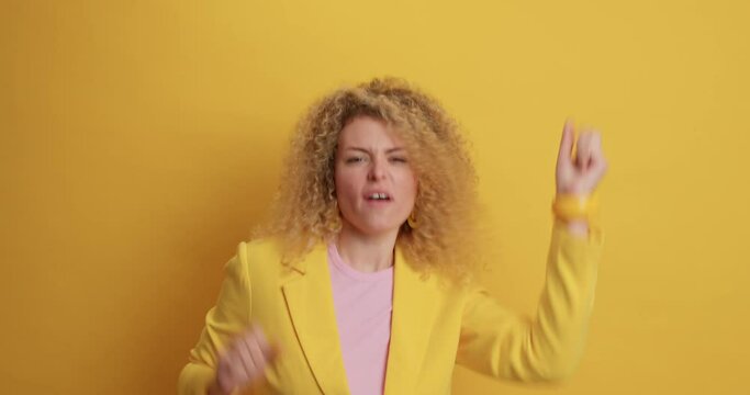 Overjoyed curly haired European woman dances happily raises arms jumps from joy has upbeat mood wears elegant clothes celebrates success smiles broadly being in good mood. Happiness concept.
