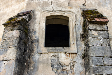 A window in the wall of a historic building. Damaged facade of the chapel in the cemetery.