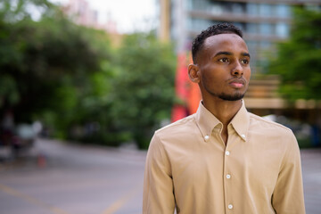 Portrait of handsome black young African businessman thinking outdoors in city