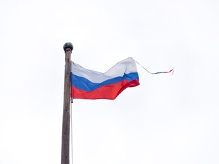 The white-blue-red flag of the Russian Federation flutters in the wind on an old wooden flagpole on...