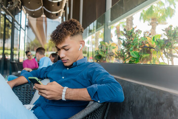 Joven latino escuchando musica y escribiendo en el celular sentado en el sof√°.