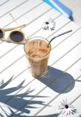 Ice coffee Cyprus Frappe Fredo top view on white table, with sunglasses. Summer minimalistic background, holiday or vacation concept. Sun and shadows.Copy space.