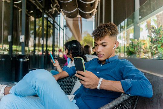 Joven latino escuchando musica y escribiendo en el celular sentado en el sof&radic;&deg;.