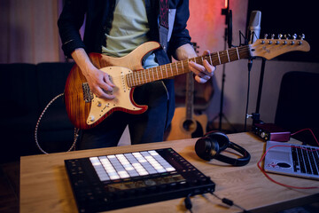 Close up of male musician playing guitar and using dj controller for mixing sounds. Man with modern equipments creating new music at studio.