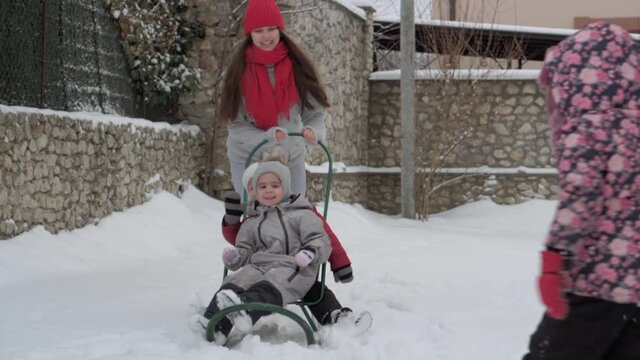 vacation, game, family concept - slo-mo authentic three happy preschool toddler kids siblings with young wonan mom sledding and play with snow. snowfall in cold season weather in winter yard outdoors