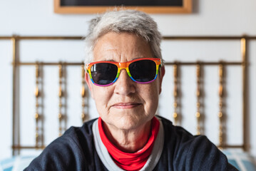 portrait of lesbian older lady with short gray hair wearing rainbow gay pride flag sunglasses.