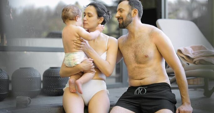 Young family relaxing with a little baby boy at spa, sitting in the hot vat outdoors. Family on vacation with a child
