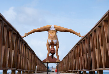 Flexible female circus doing handstand upside down on the pier with sky background. Individuality,...