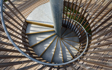 Top view of a magnificient metal spiral staircase inside a wooden structure illuminated by the sun.