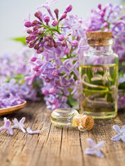 Spa oil with lilac flowers. A bottle with aromatic oil and lilac flowers on a wooden background.copy space