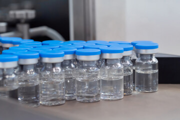 Many medical injection glass vials with blue tops and liquid - close up, selective focus. Pharmaceutical industry, medicine and laboratory equipment concept