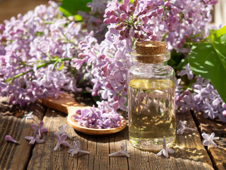 Fototapeta na wymiar Spa oil with lilac flowers. A bottle with aromatic oil and lilac flowers on a wooden background.copy space