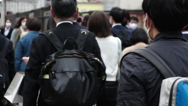 OSAKA, JAPAN - APRIL 2021 : Back shot and unidentified crowd of people wearing surgical masks to protect from Coronavirus (COVID-19) at the street. Slow motion shot. In front focus.