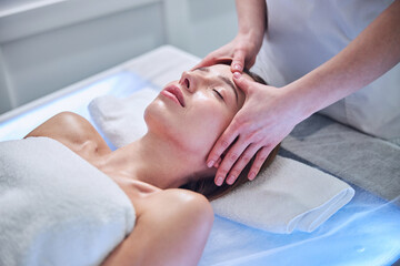 Fototapeta na wymiar Pretty Caucasian female lying on massage table while enjoying spa procedure in spa center