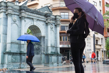 Mujer joven con un paraguas hablando por telefono en un dia lluvioso
