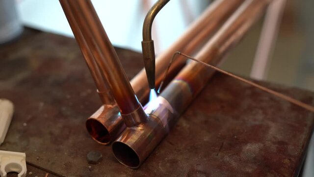 Close up on hands of unknown industrial worker plumber with central heating copper pipes welding using gas torch or blowtorch at work