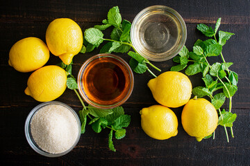 Kentucky Lemonade Cocktail Ingredients: Bourbon, sugar, mint, and lemons on a dark wood background