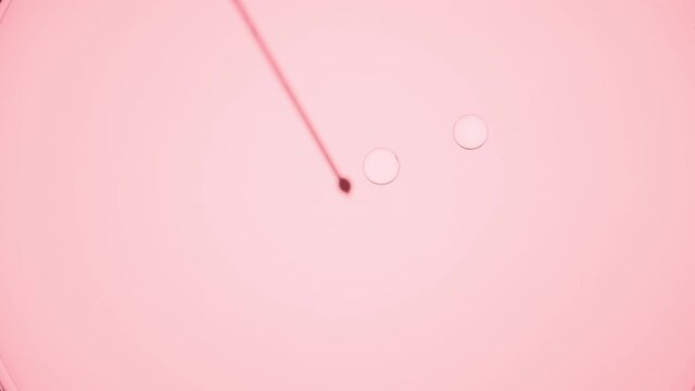Clear small drops are injected into clear liquid from syringe against pale pink background | Macro shot of body care balm for its commercial