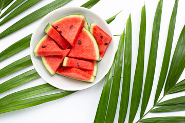 Watermelon slices in white plate on tropical palm leaves on white