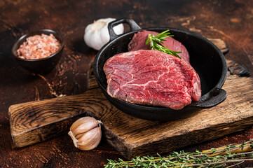 Raw Tenderloin beef fillet meat in a pan with herbs. Dark background. Top view
