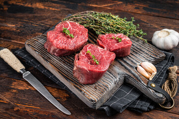 Prime raw Fillet mignon steaks on a wooden board with thyme and garlic. Dark wooden background. Top...