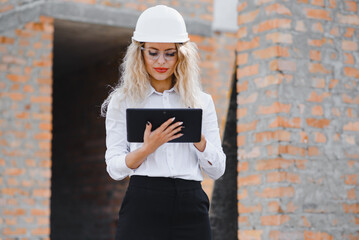 Absorbed in the work of a woman engineer working with a tablet on the background of the construction site. Portrait of a young architect, protective equipment. Selective focus.