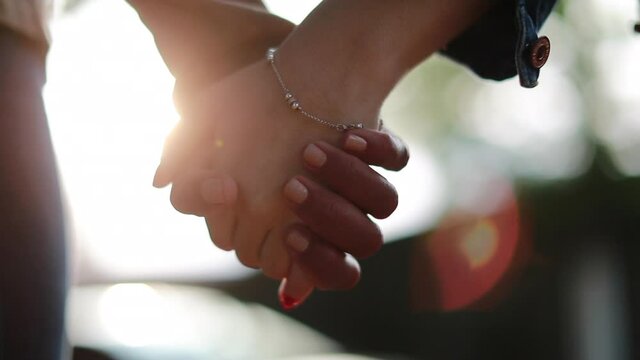 Two diverse people holding hands, close-up in sunlight