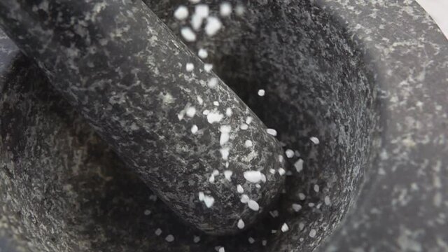 Close-up of the sea salt falling and bouncing in the grey stone mortar
