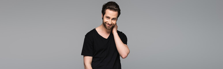 shy bearded man in black t-shirt smiling isolated on grey, banner.