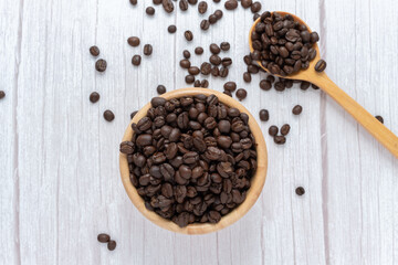 Coffee beans in wooden cup and spoon on wooden floor background.