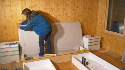 CLOSE UP: Young woman moving into her house unpacks the headboard of her bed.