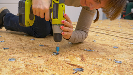 CLOSE UP: Female worker screwing thin metal discs in place on a plywood panel.