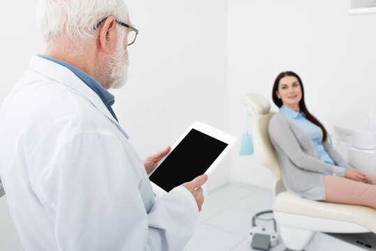 senior dentist standing with tablet in front of patient in dental clinic.