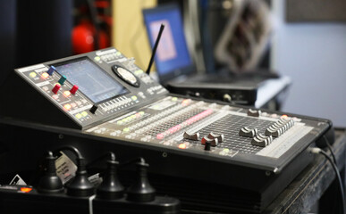 A small sound engineering studio mixing deck board and laptop in the background. Board with multiple lights, switches, dials and level adjustments for laying down tracks and calibrating sound.