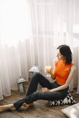 Girl in an orange jacket sits on floor and drinks juice