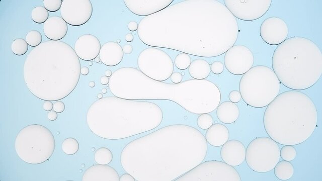 Pale grey different sized stretched bubbles take round shape against cyan background | Macro shot of skin care cream with hyaluronic acid ingredients for its commercial