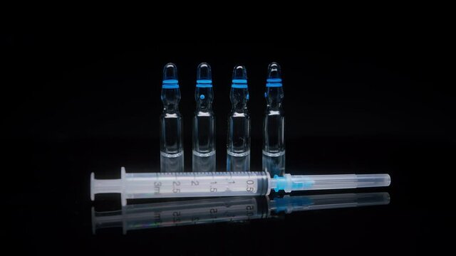 Close-up of syringe and ampoules with vaccine against coronavirus. Showing sample of medicine on black background, vaccination against covid-19, laboratory research concept. 