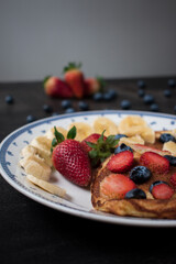 Some pancakes with sweet strawberry, blueberry and banana sliced on black table with some fruit on it 