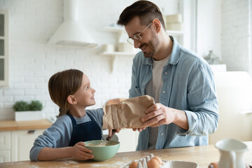 Happy loving young Caucasian father teach small 7s daughter baking preparing dough in kitchen together. Smiling caring dad and little girl child cook at home sweet cookies or pie. Parenthood concept.